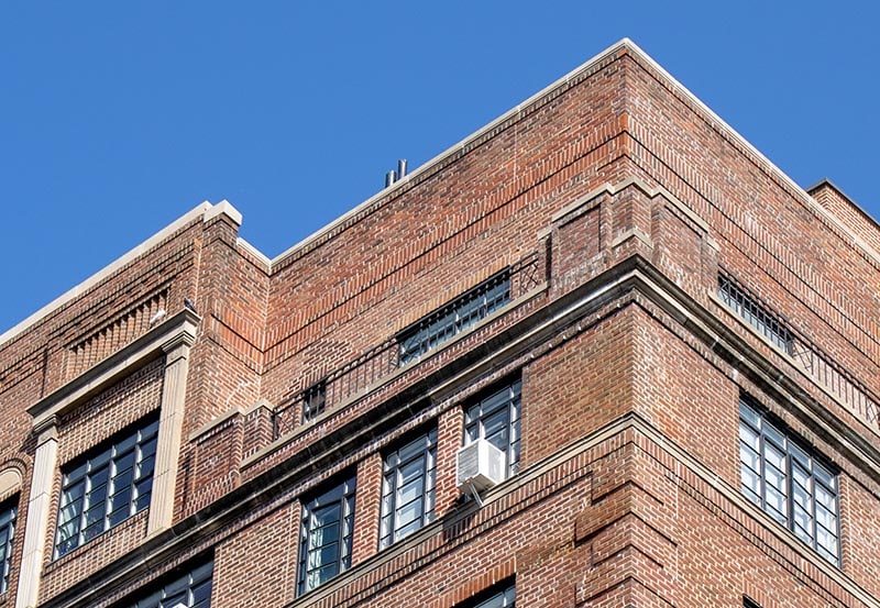 A low-angle shot of the upper exterior of a multi-story brick building set against a clear blue sky.
