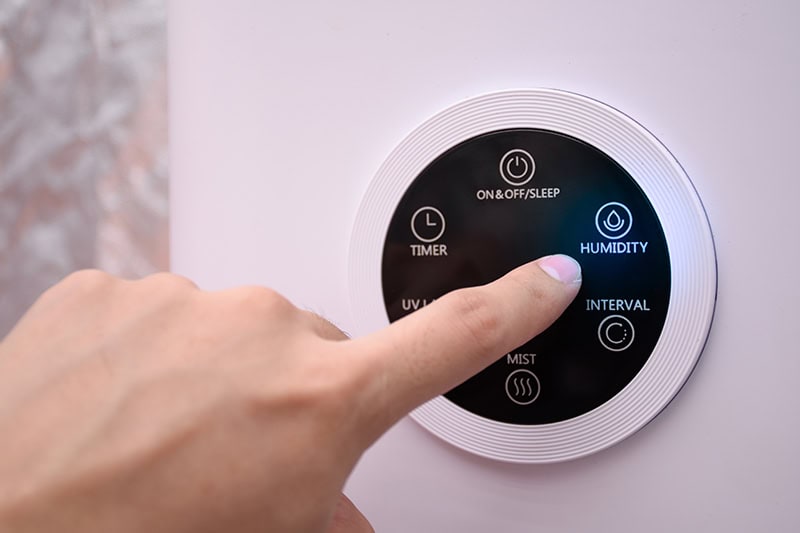 Close up of a hand pressing the digital humidifier button on a smart thermostat.