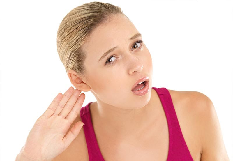 A close-up shot of a young woman gesturing to hear something against a plain white background.